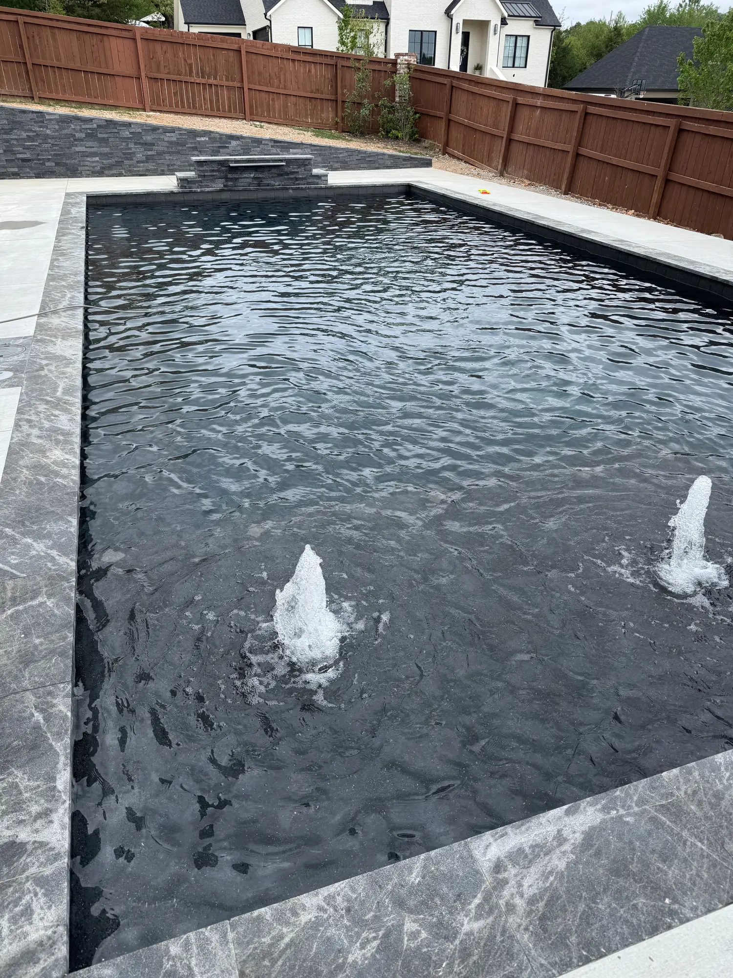 Black-bottom pool with bubbler water features and marble decking in Northwest Arkansas