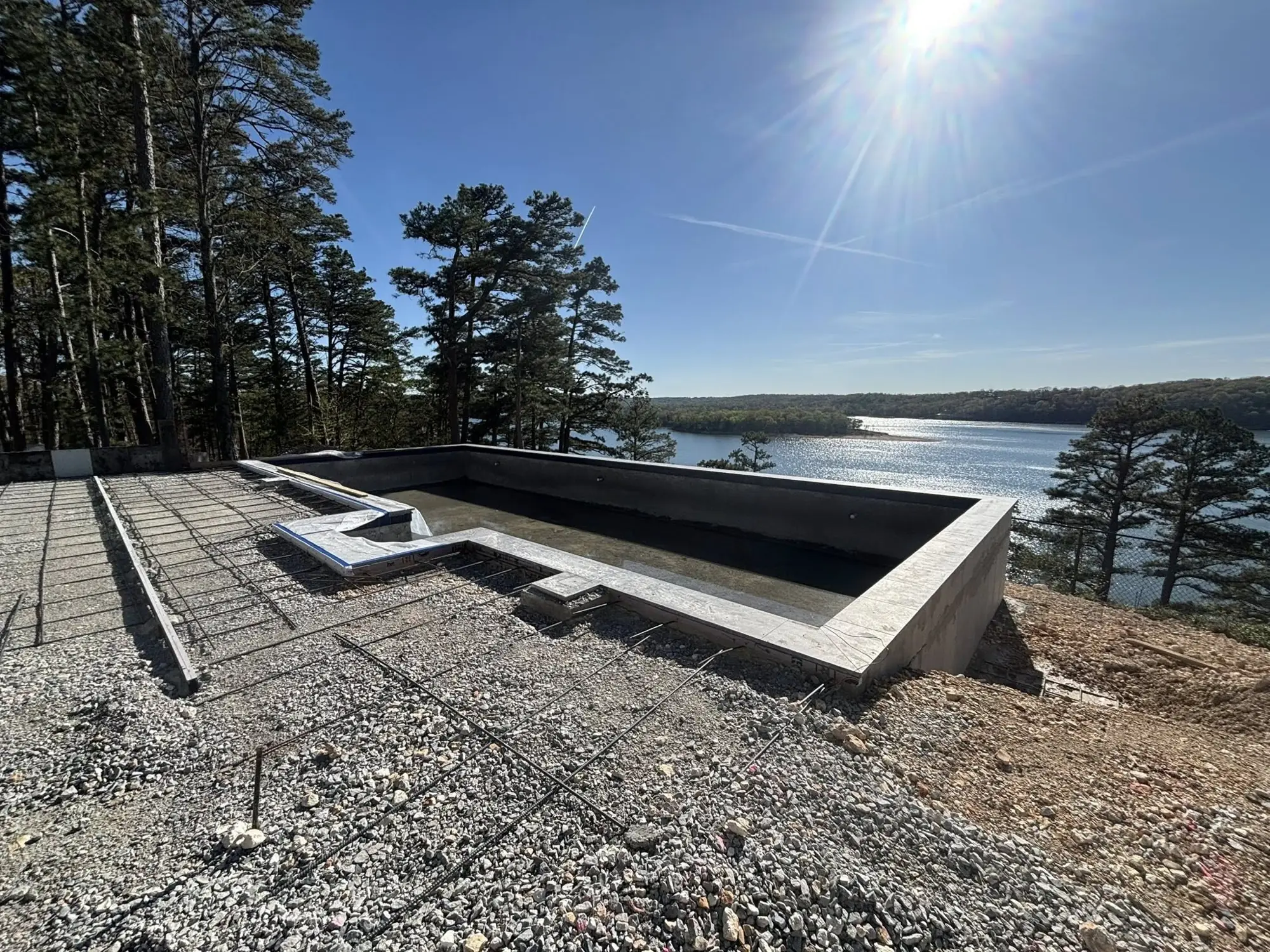 Infinity-edge pool shell under construction overlooking a lake in Northwest Arkansas
